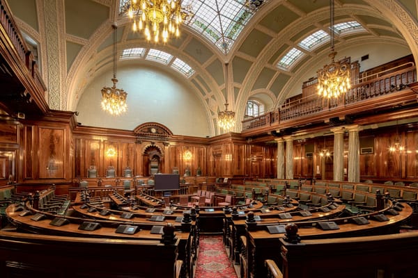 Ornate council chamber with wood paneling, chandeliers, and many seats